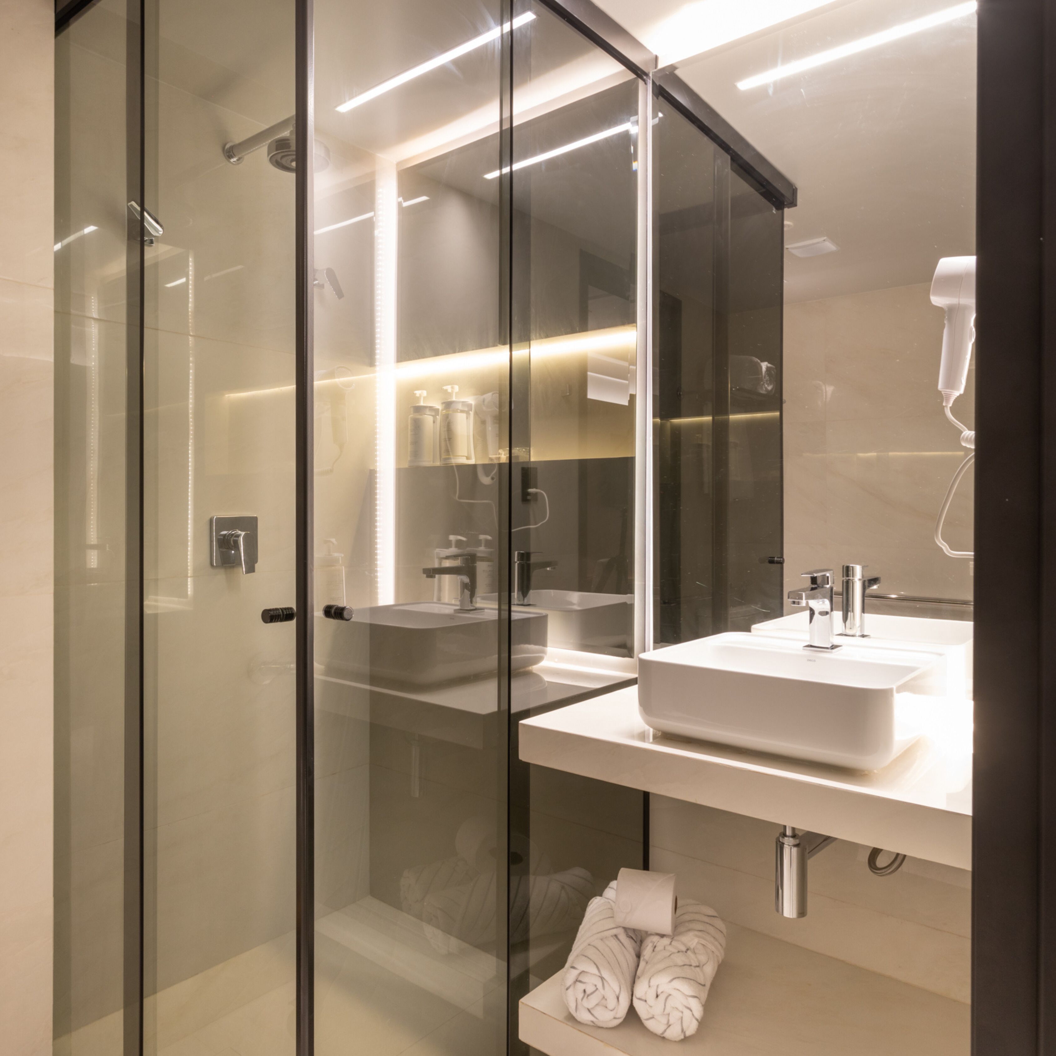 A modern bathroom with a glass shower enclosure, a large mirror, and a white sink.