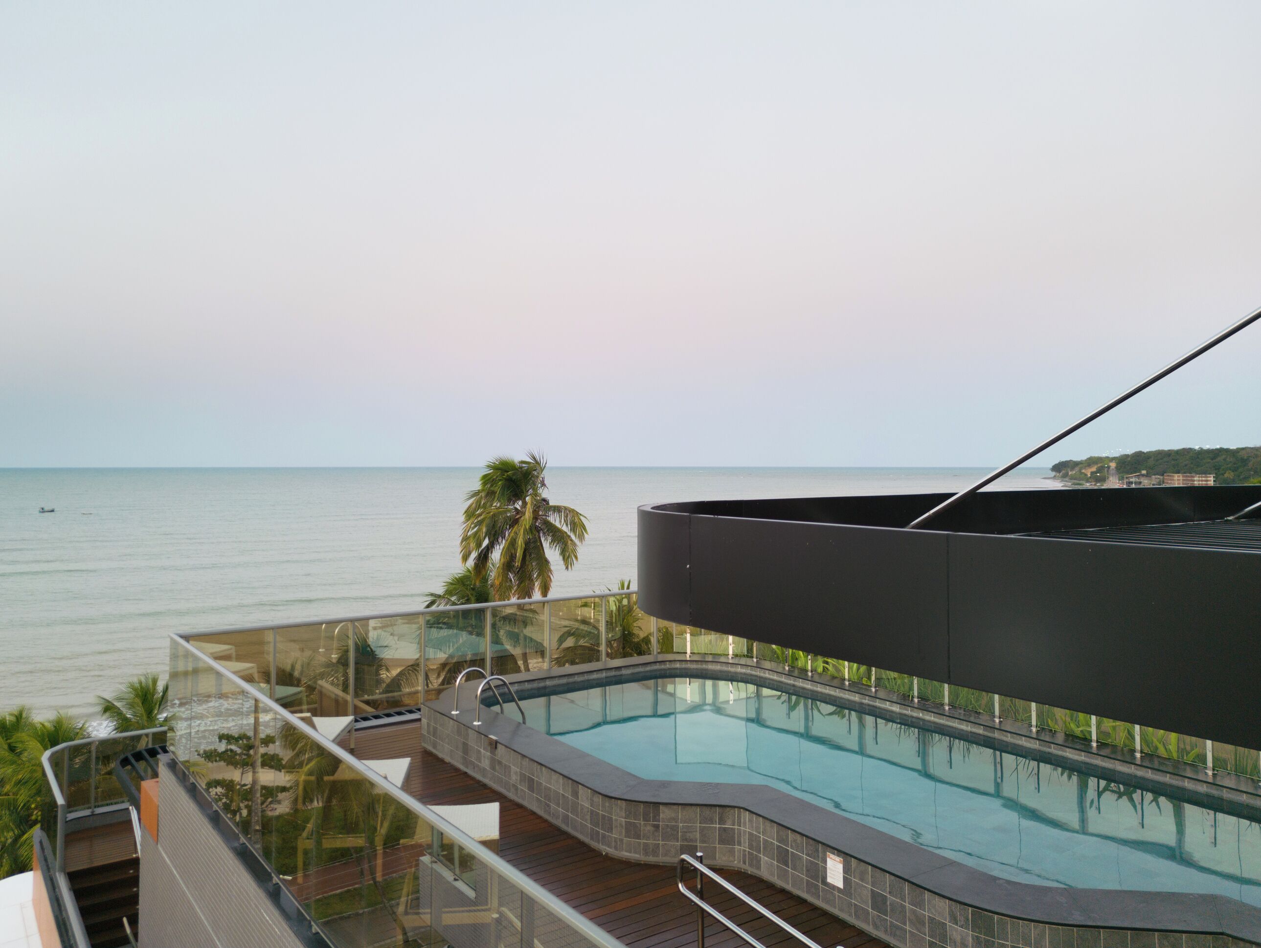 Een modern zwembadgedeelte met een glazen balustrade, een golvend zwembad en uitzicht op de zee.