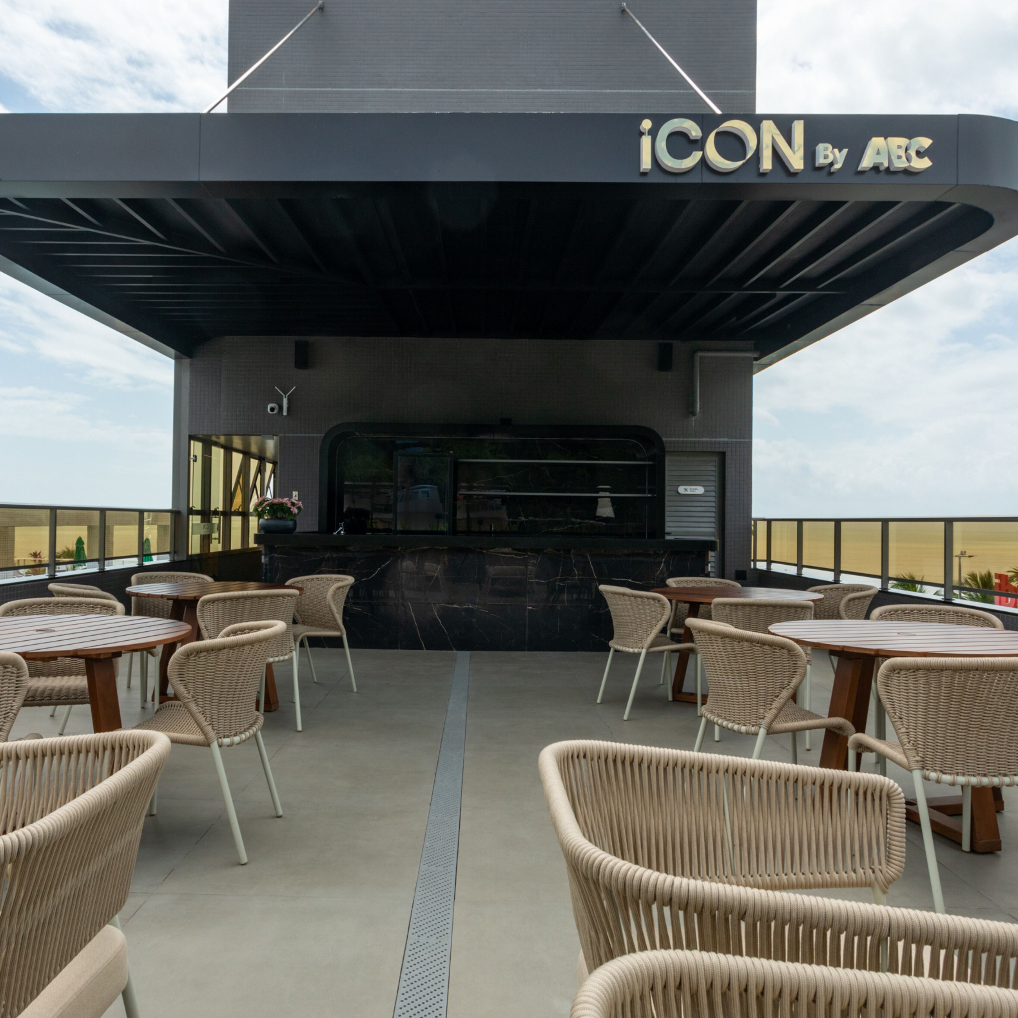Un espace extérieur aménagé avec des chaises et des tables en osier, un comptoir de bar et une enseigne indiquant « ICON By ABC ».
