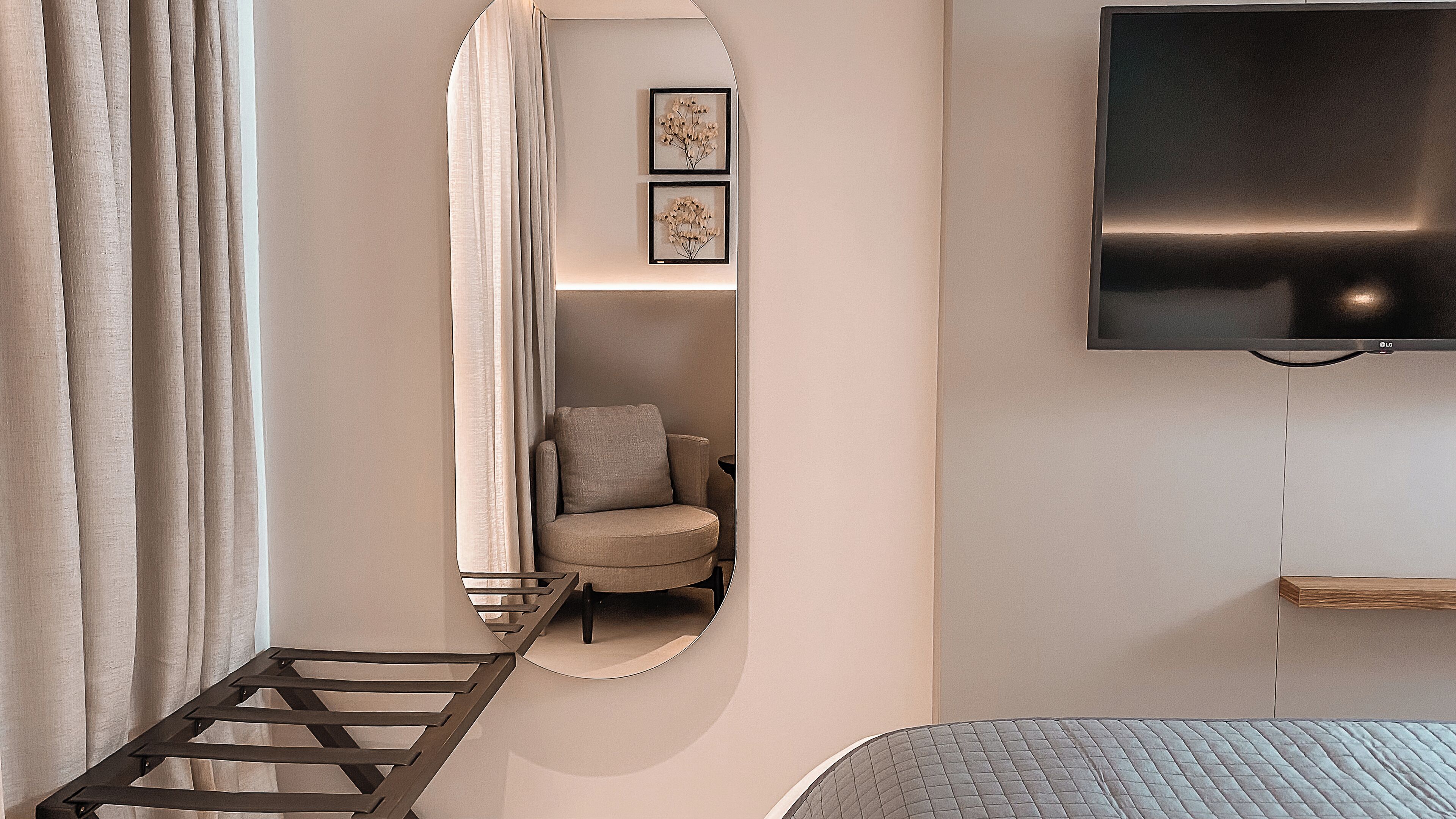 Een slaapkamer met een bed, een aan de muur bevestigde televisie, een stoel en een klein plankje.