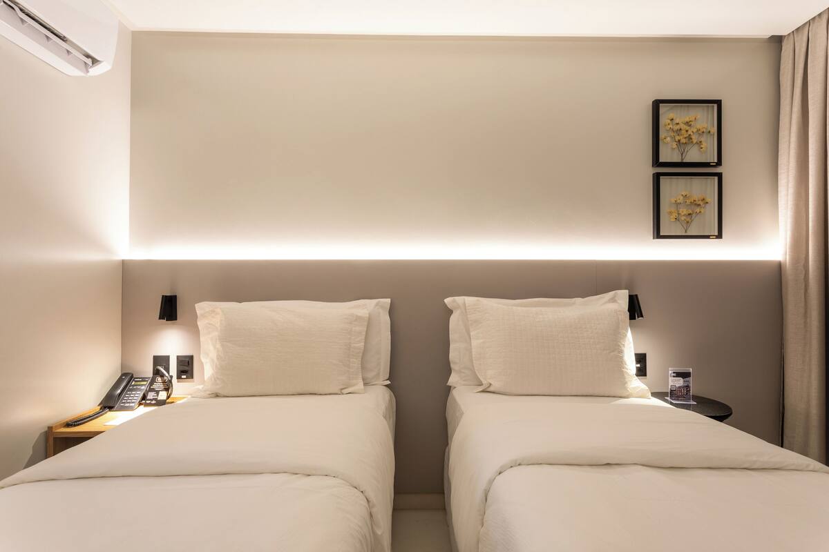 A hotel room with two beds, a bedside telephone, a nightstand, and a wall-mounted light fixture.