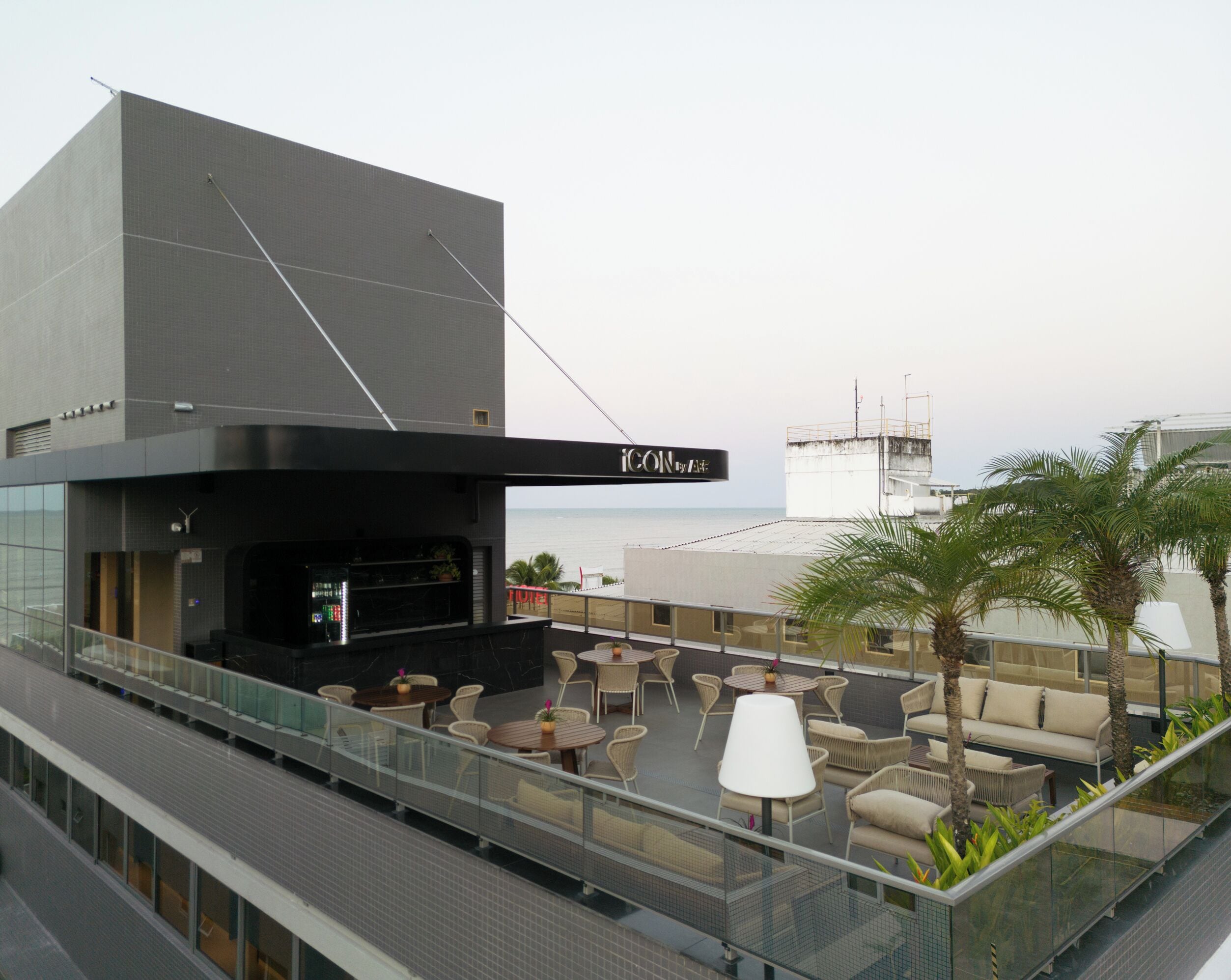 Um bar no terraço com área externa, vista para o mar e estrutura de prédio moderna.