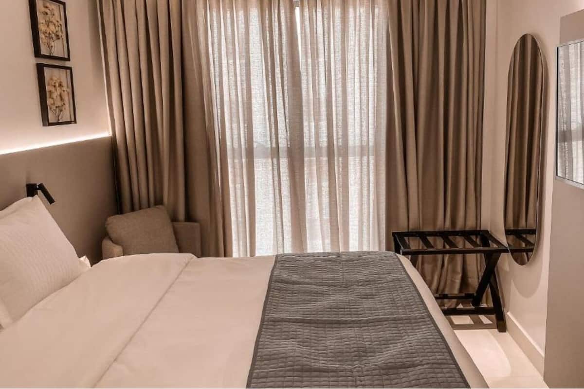 A hotel room with a bed, a bedside table, a wall-mounted TV, and a window with curtains.