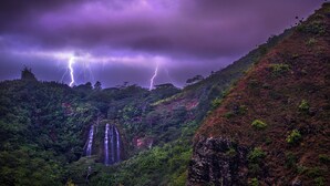 Una cascada se precipita por una ladera verde y exuberante bajo un cielo tormentoso.