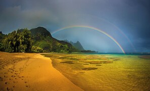 Une plage avec un arc-en-ciel, une eau cristalline et une montagne en arrière-plan.