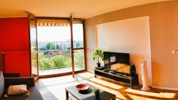 Een moderne woonkamer met een grote televisie, een bank, een kleine tafel en een schuifdeur naar een balkon.