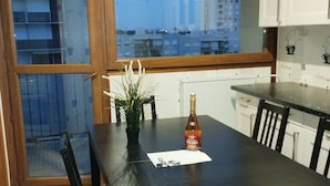 Een eetgedeelte met een donker houten tafel, witte stoelen, een fles wijn en een potplant.