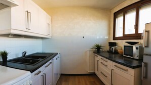 Een kleine keuken met witte kastjes, een zwart aanrecht, een spoelbak, een magnetron en een koelkast.