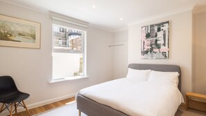 A bedroom with a bed, a chair, a window, and artwork on the walls. - Host Stay Prince Albert (Margate)