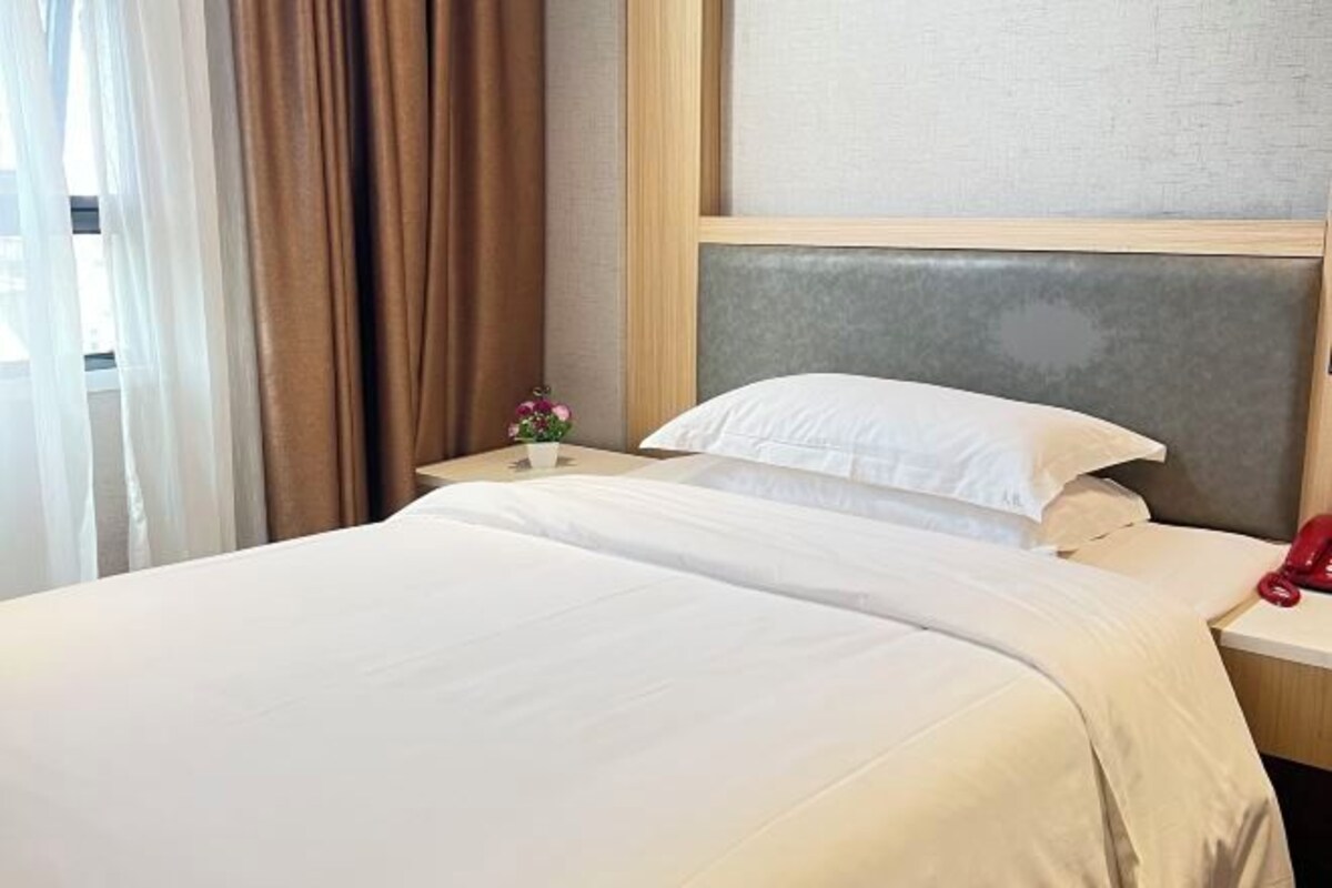 A hotel room with a bed, a nightstand, a telephone, and a window with curtains.