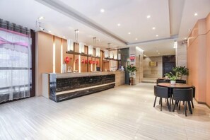 A hotel reception area with a marble floor, a reception desk, a seating area with a table and chairs, and a large window with curtains. - Guangzhou Jiulong Hotel (Sansui Fuzheng West Road Branch) (Sansui)
