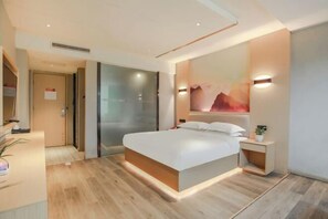 Een moderne slaapkamer met een groot bed, nachtkastjes, een muurlamp en een deur met een bordje.
