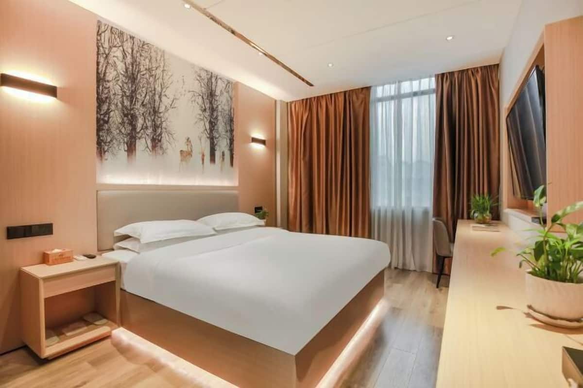 Een moderne hotelkamer met een groot bed, nachtkastjes, een bureau en een groot raam met gordijnen.