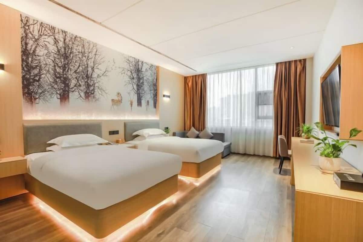 Een hotelkamer met twee bedden, een bureau, een groot raam met gordijnen en een kunstwerk aan de muur.