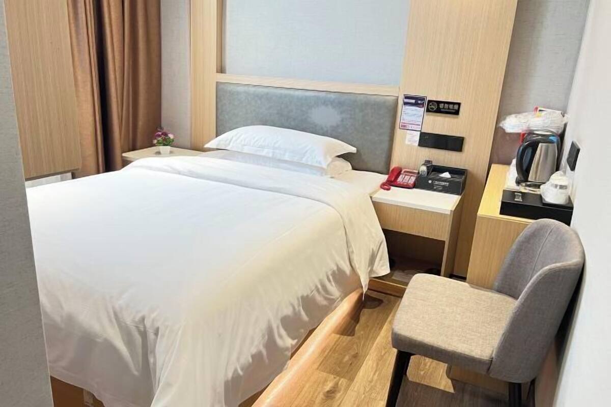 Una habitación de hotel con una cama, una mesita de noche con lámpara, una silla y un escritorio pequeño con teléfono.