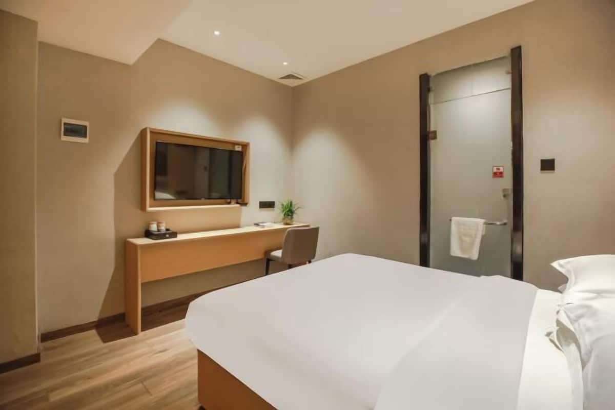 Een hotelkamer met een bed, bureau, stoel, spiegel en een deur.
