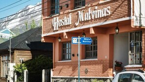 Egy „Hostal Malvinas” nevű szálláshely, amelynek téglafalas homlokzata van, egy tábla jelzi, hogy ez egy hostel, és a háttérben egy hegy látható.