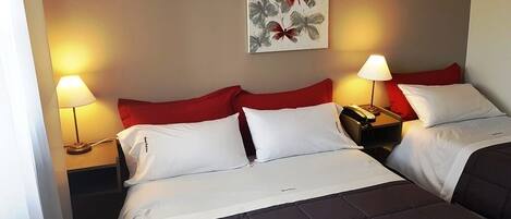 Une chambre d’hôtel avec deux lits, chacun agrémenté de draps rouges et blancs, une table de chevet avec une lampe et une œuvre d’art accrochée au mur.