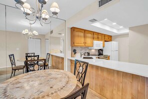 A modern kitchen with wooden cabinets, a white countertop, and a dining area with a mosaic table and chairs.