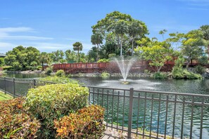 A tranquil pond with a fountain, surrounded by lush greenery and a wooden bridge.