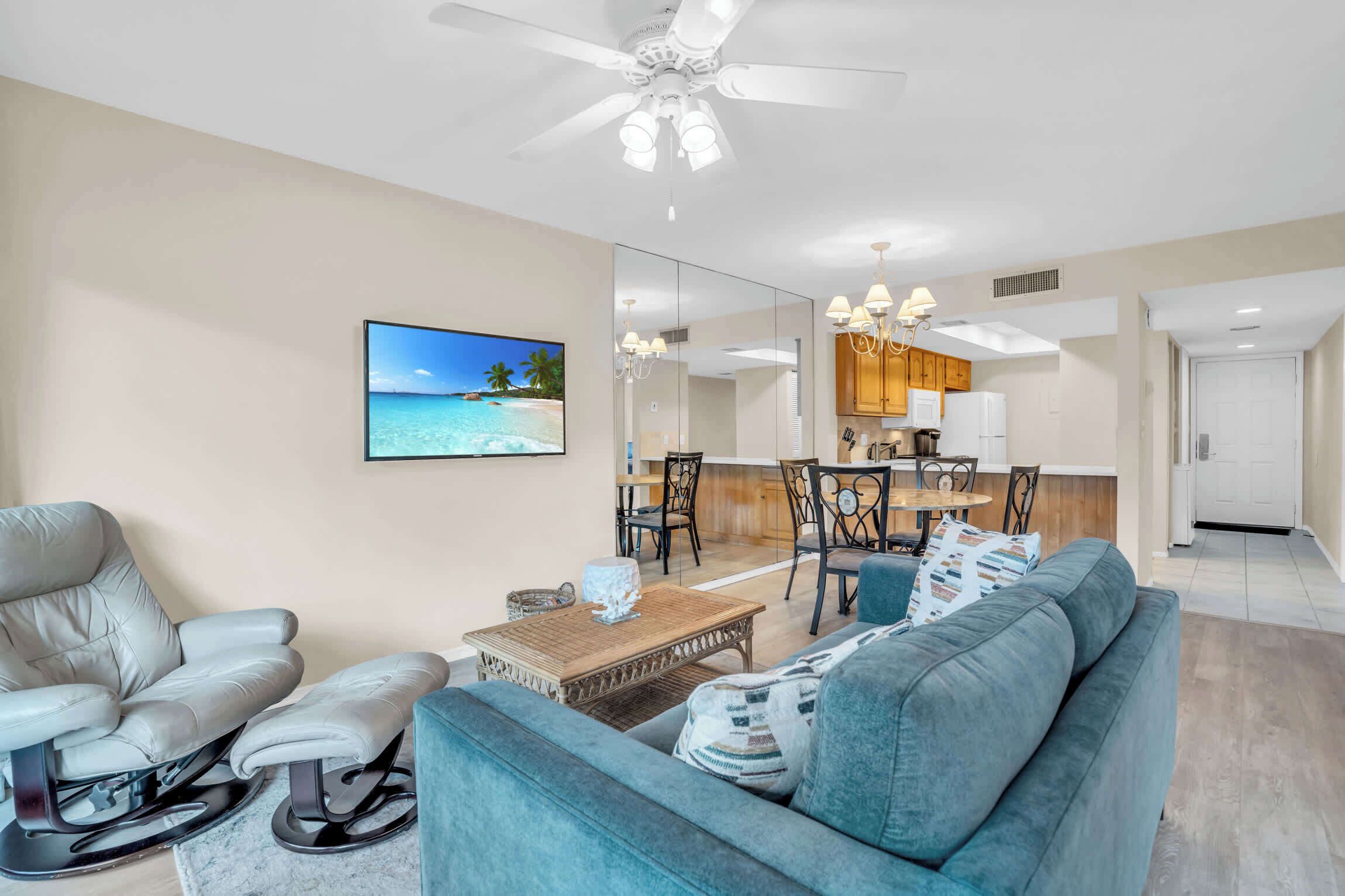 Una sala de estar moderna con un sofá, un sillón reclinable, una mesa de centro y un televisor que muestra una escena de playa.