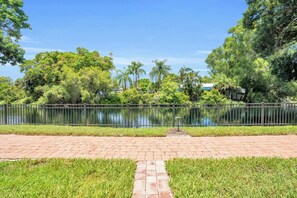 A paved walkway beside a calm body of water, surrounded by lush greenery and a metal fence. - G-143 - First Floor With Lake Views -Sleeps 6 (Naples)