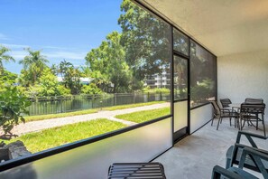 A balcony with a view of a lake, a grassy area, and a building in the background.