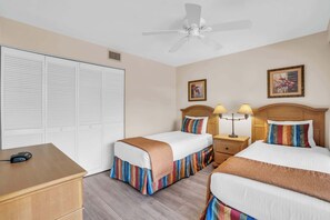 A hotel room with two beds, a desk, a wardrobe, and a ceiling fan.