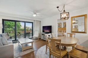 A modern living room with a dining area, large sliding glass doors to a balcony, a flat-screen TV, and a chandelier. - E-233 - Deluxe Condo with Lake Views & Sleeps 6 (Naples)