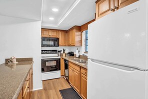A modern kitchen with wooden cabinets, a white refrigerator, a microwave, an oven, and a dishwasher. - E-233 - Deluxe Condo with Lake Views & Sleeps 6 (Naples)