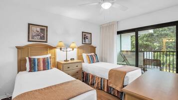 Habitación de hotel con dos camas, ventilador de techo y balcón con vista a zonas verdes.