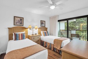 Habitación de hotel con dos camas, ventilador de techo y balcón con vista a zonas verdes.