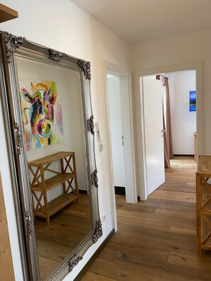 Un couloir orné d’un grand miroir décoratif qui reflète une peinture aux couleurs vives, des meubles en bois et une porte donnant sur une autre pièce.