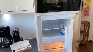 Een compacte keuken met een ingebouwde magnetron, een koffiezetapparaat en een koelkast met overzichtelijke opbergbakken.
