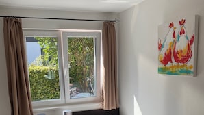 Een hotelkamer met twee enkele bedden, een nachtkastje met een lamp, een raam met gordijnen en een schilderij aan de muur.