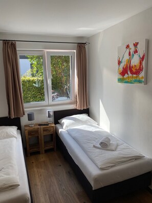 Een hotelkamer met twee bedden, een raam met gordijnen, een nachtkastje met lampen en een schilderij aan de muur.