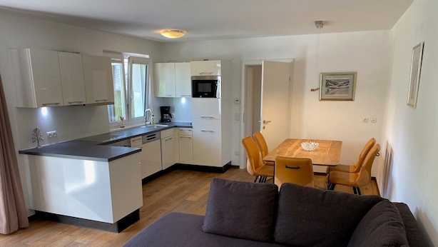 Een knus woongedeelte met een kitchenette, een eethoek met tafel en stoelen, en een bank.