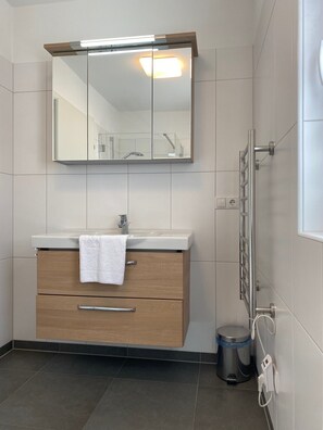 Een moderne badkamer met een houten wastafelmeubel, een grote spiegel en een handdoek aan de rand.