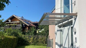 Een modern gebouw met een glazen ingang, een heldere lucht en een traditioneel huis op de achtergrond.