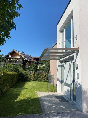 Een modern huis met een glazen deuropening, een overdekt terras en een verzorgd gazon.