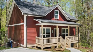 A red single-story house with a front porch, a small staircase, and a garage. - Babbling Brook-New construction (Maggie Valley)