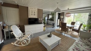 A spacious living room with a white sofa, a white coffee table, and a dining area with wicker chairs. - Apartment LA BASTIDE (Rosières, Haute-Loire)