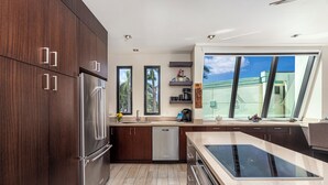 A modern kitchen with dark wood cabinets, stainless steel appliances, and a large window providing a view of the sky. - Puu Poa 407: 2  BR, 2  BA Condominium in Princeville, Sleeps 4 (Princeville)