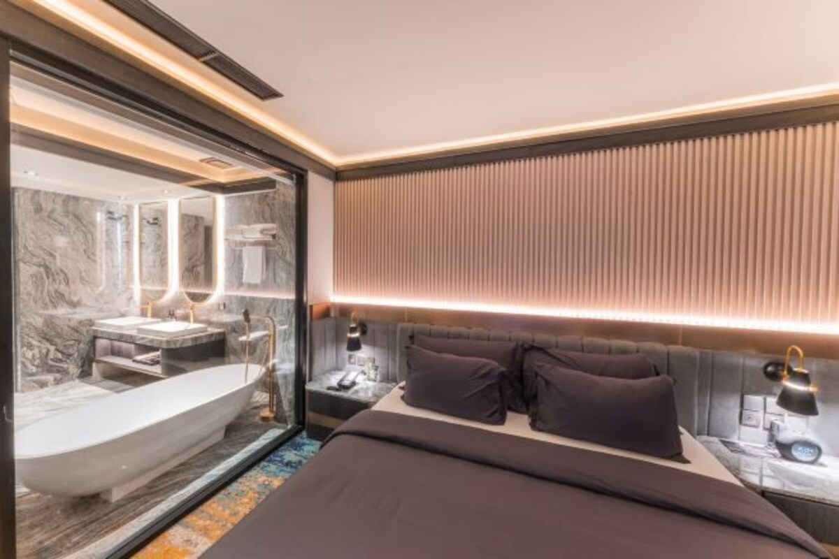 Quarto de hotel moderno com uma cama grande, uma banheira integrada e um espelho amplo.