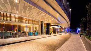 Een modern hotel aan de buitenkant bij nacht, met een gebogen gevel, een terras en een goed verlichte ingang.