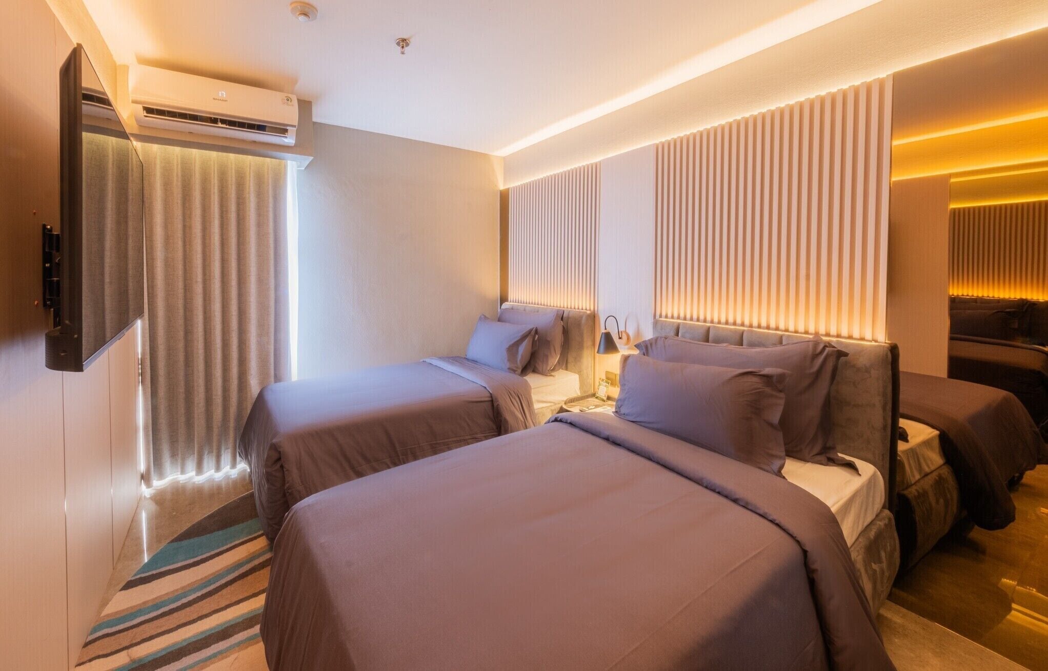 Une chambre d’hôtel avec deux lits, un téléviseur à écran plat fixé au mur, un appareil de climatisation et un tapis à rayures.