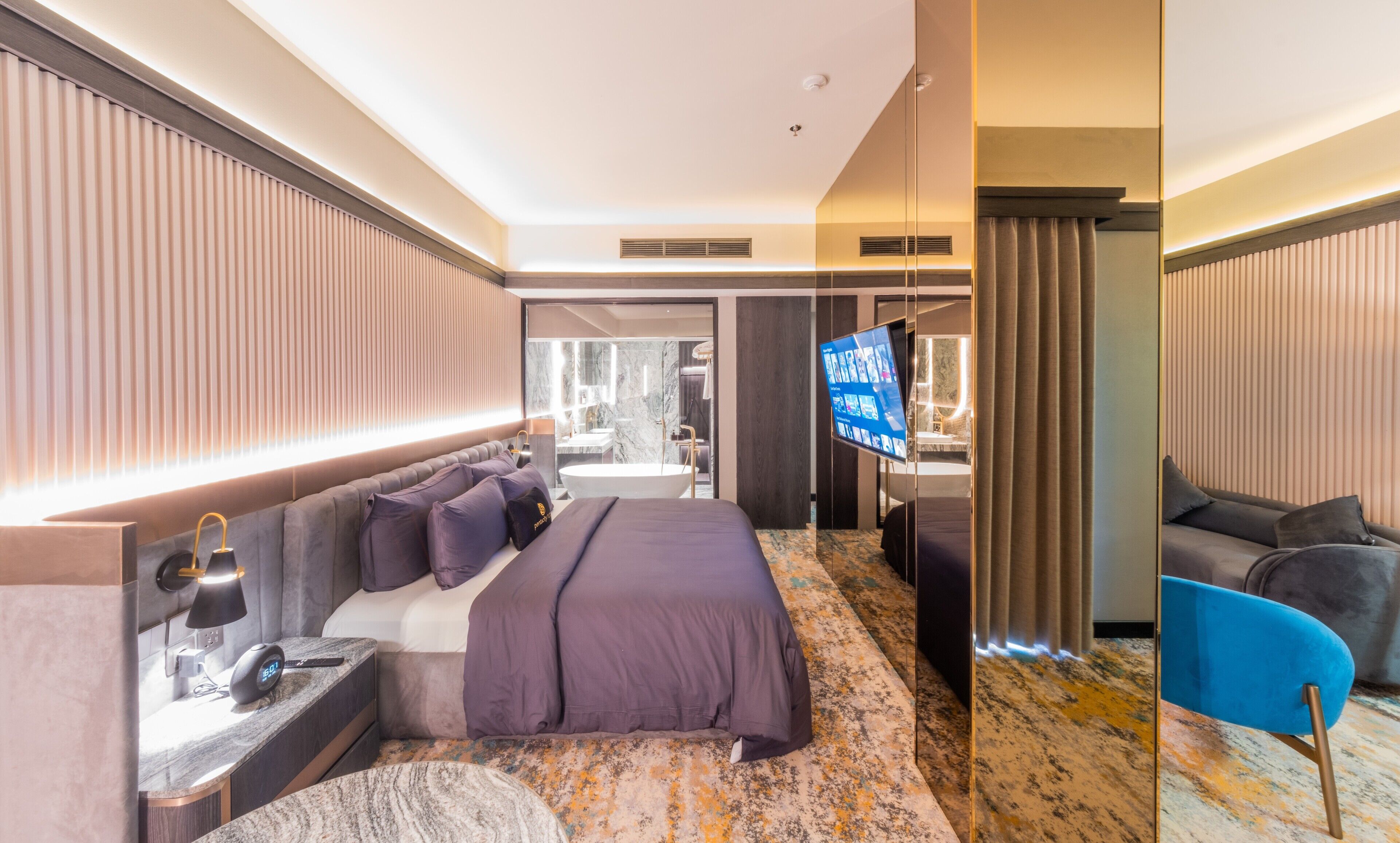 Ein modernes Hotelzimmer mit einem großen Bett, einem Fernseher, einem Schreibtisch mit Lampe und einem durchgehenden Türspalte sichtbaren Badezimmer.