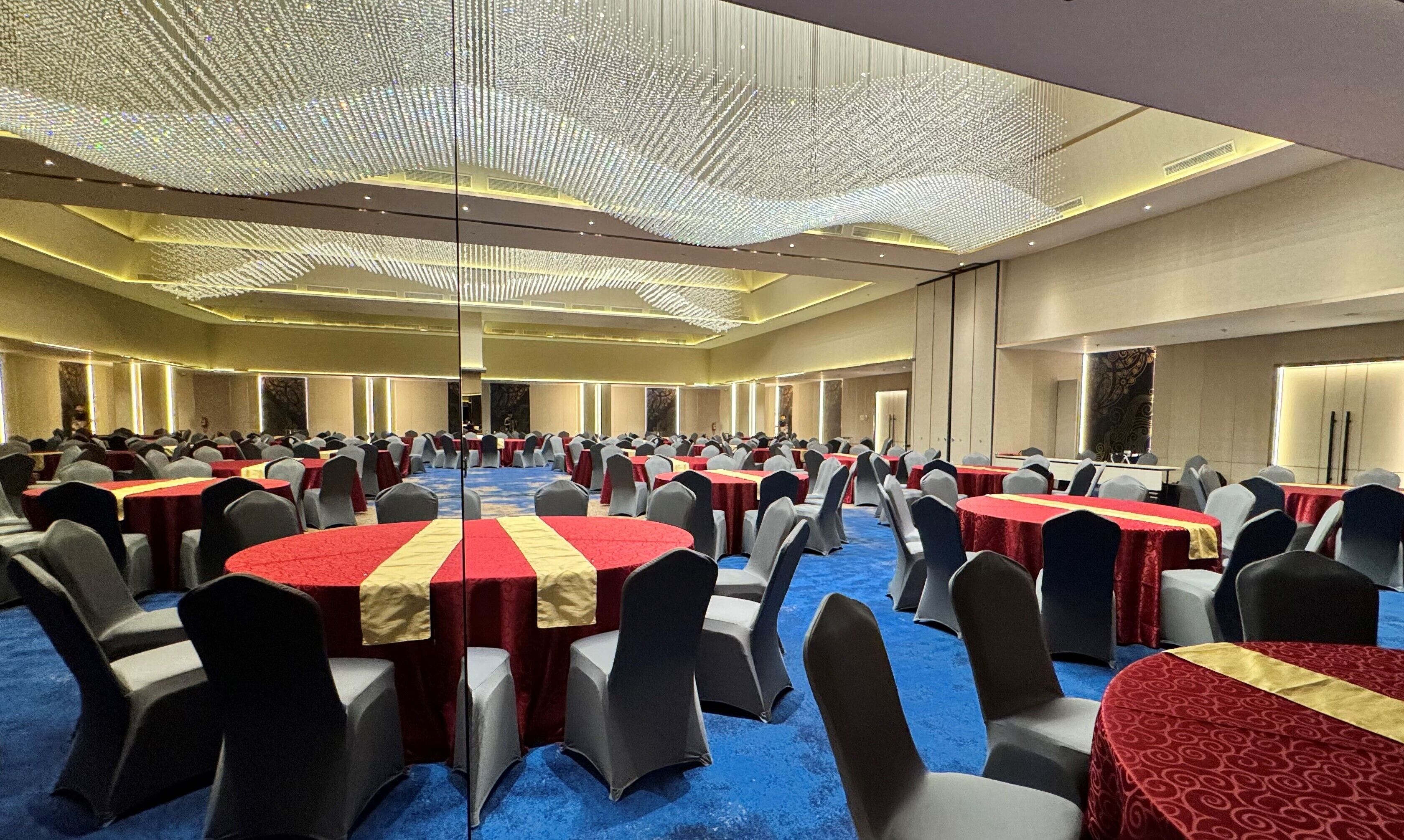 A large conference room with round tables, grey chairs, and red tablecloths.