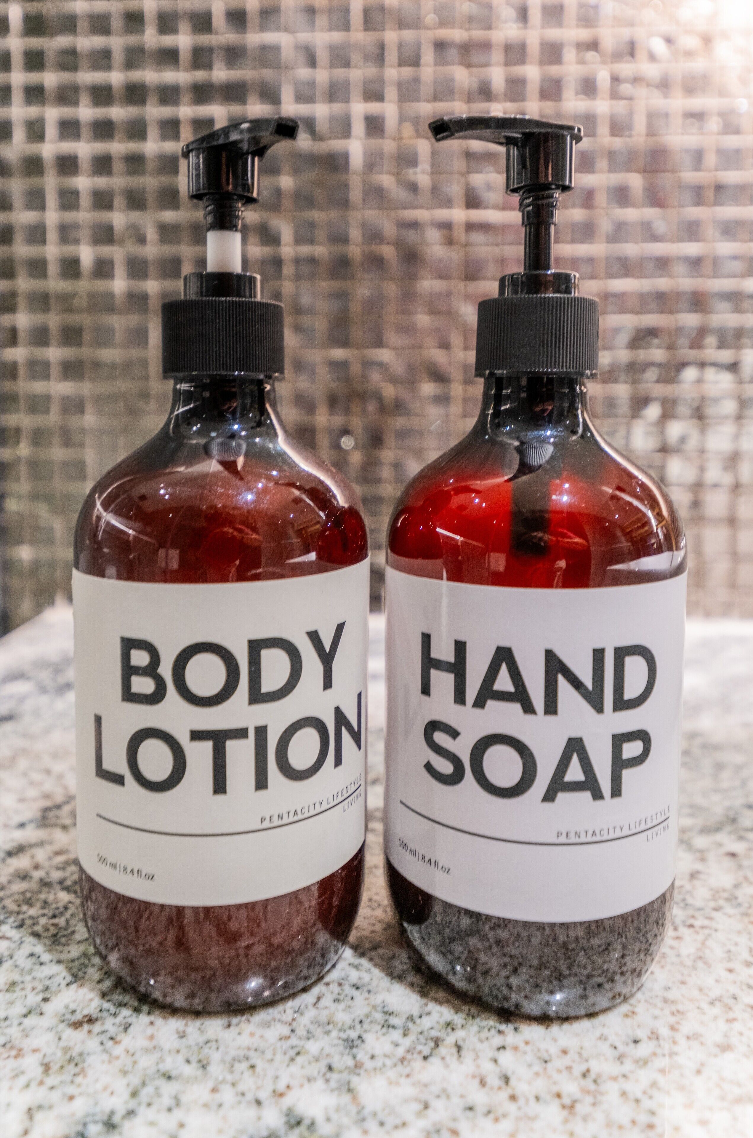 Two bottles of body lotion and hand soap on a marble countertop.