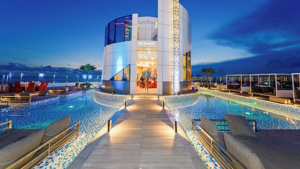 Een modern hotel met zwembad, met een centraal gebouw met een glazen gevel en een decoratief verticale element.